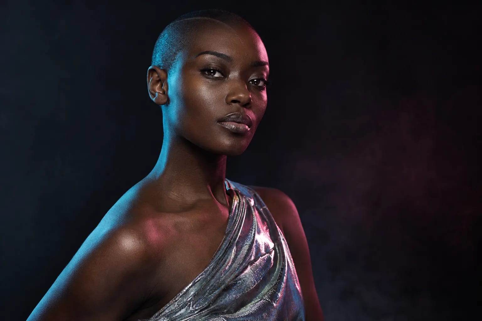 Portrait éditorial d’une femme au crâne rasé éclairée de cyan et de magenta