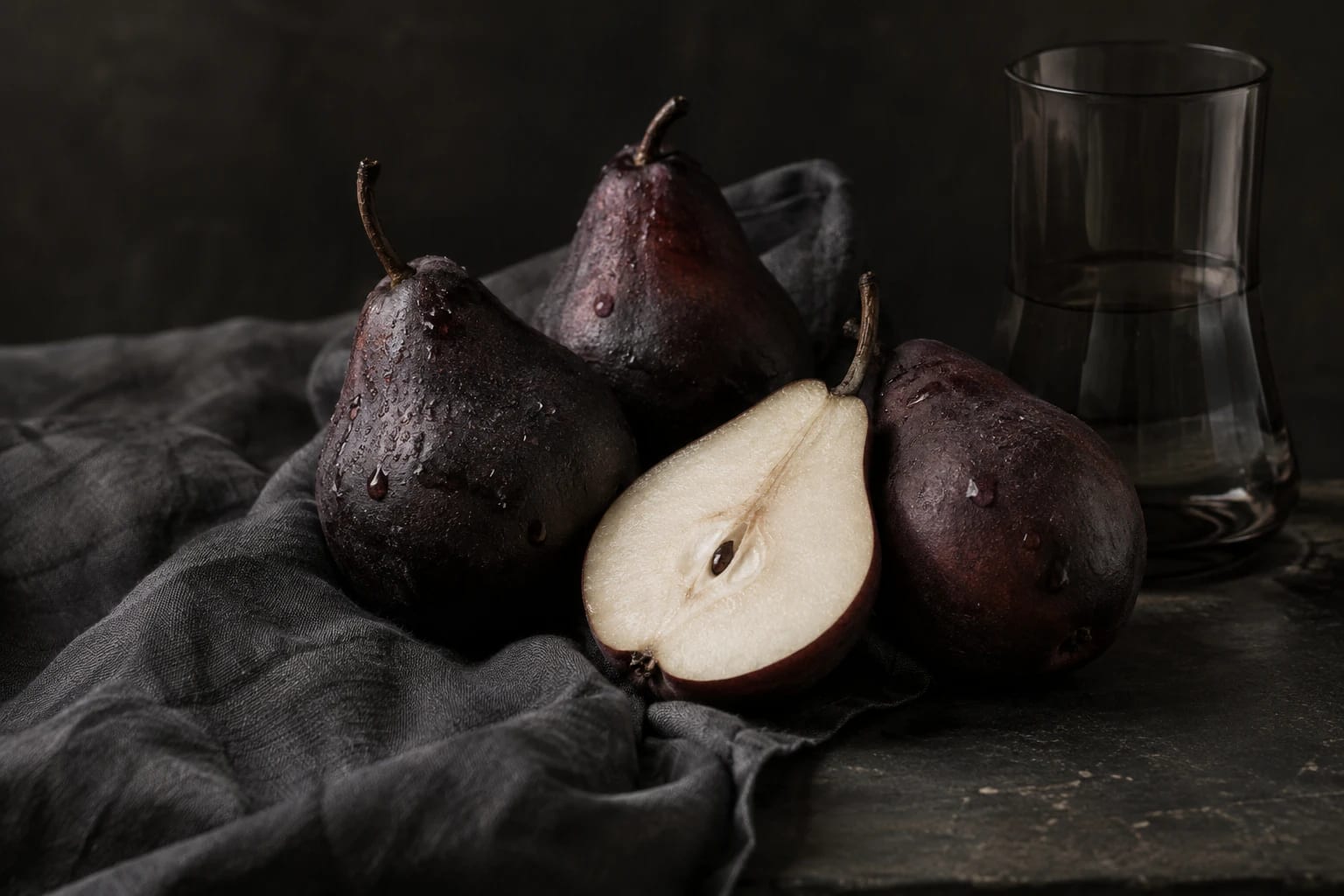Poires pourpres sur un linge graphite dans une lumière de nature morte