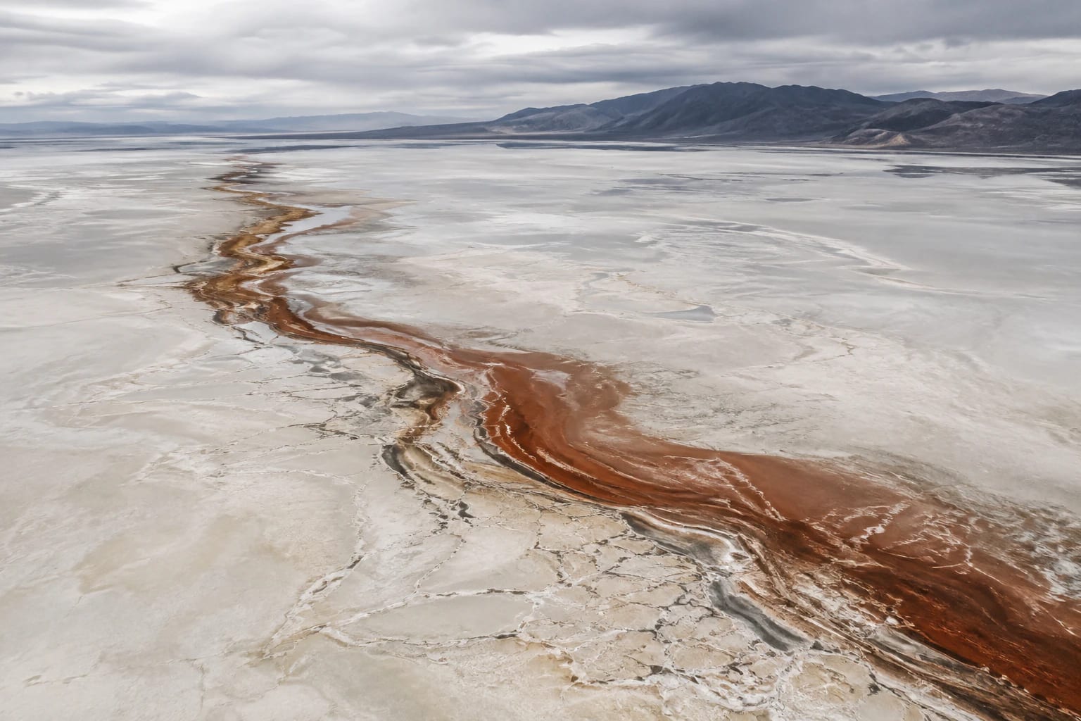 Vue aérienne de salines ivoire traversées par un chenal minéral couleur rouille