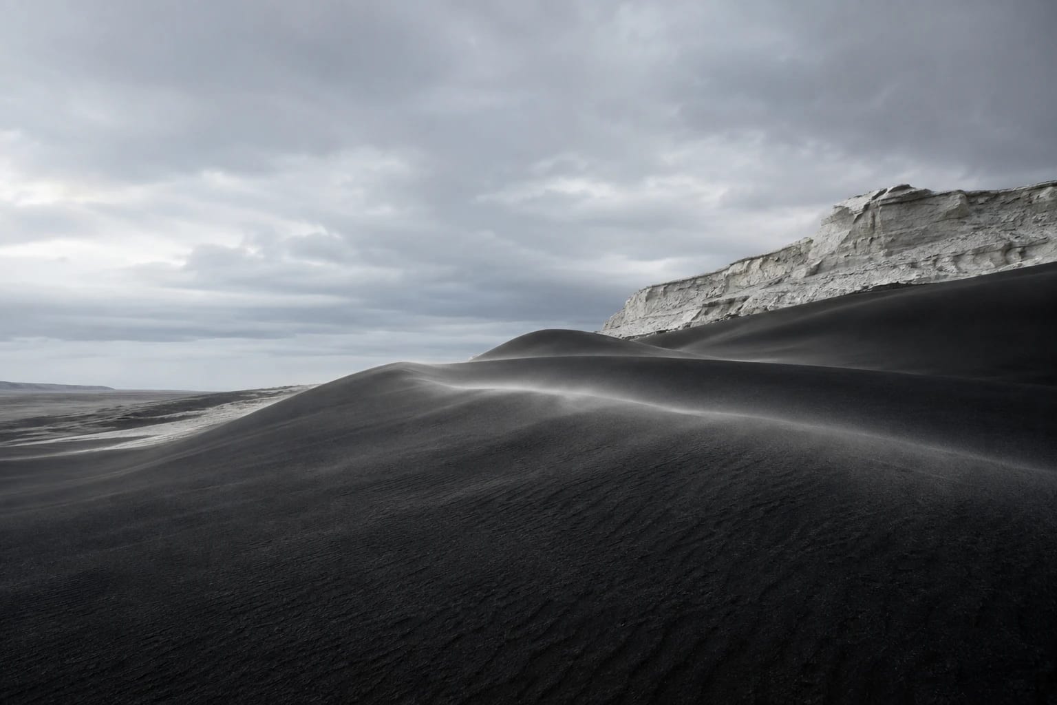 Dunes de sable volcanique noir longées par une falaise de craie